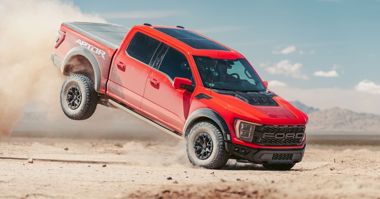 A red Ford Raptor lands after jumping an obstacle in the desert